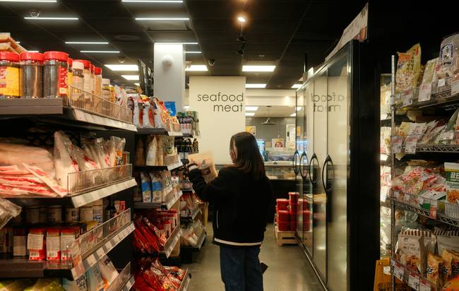 Canadian grocery shopper using a coupon app on their phone in a supermarket aisle for digital savings